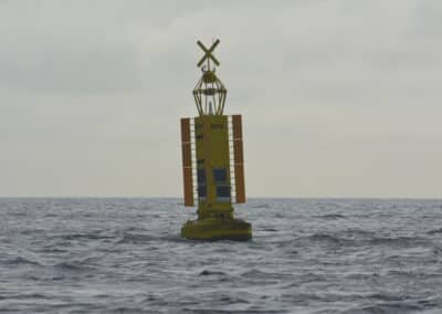 Yellow offshore navigation buoy with solar panels and an X-shaped beacon, floating in choppy sea